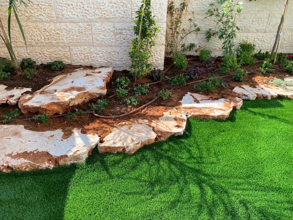 סלעים טבעיים גדולים בשפת הערוגה עם שתילים וקווי טפטוף