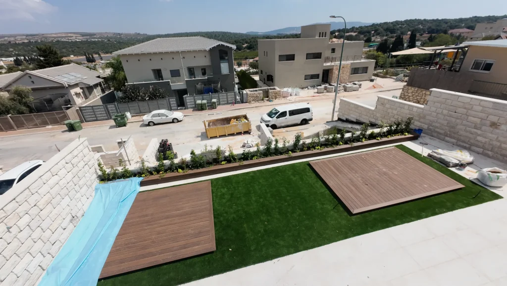 דשא סינטטי ושני משטחי דק בחצר הווילה במירון, עם ערוגה שתולה לאורך הגדר