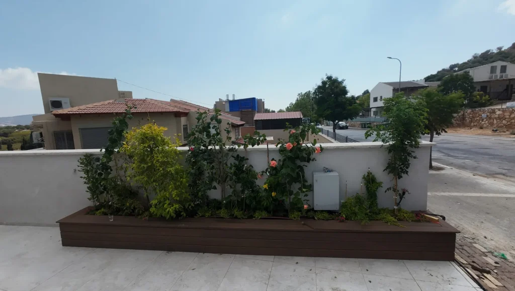 אדנית עץ עם שיחים ופרחים בפינת החצר