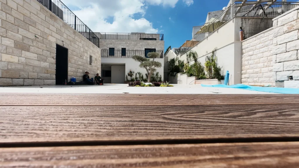 משטח הדק מקרוב, ומאחוריו החצר והבית