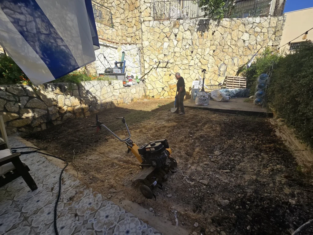 החצר לפני השתילה: אדמה מתוחחת וקלטרת מול קיר האבן