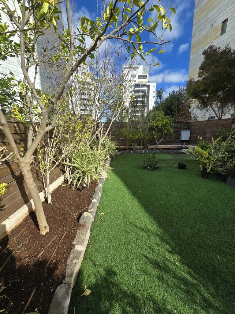 ערוגה ארוכה עם עצים צעירים ושפת אבן לאורך הדשא הסינטטי