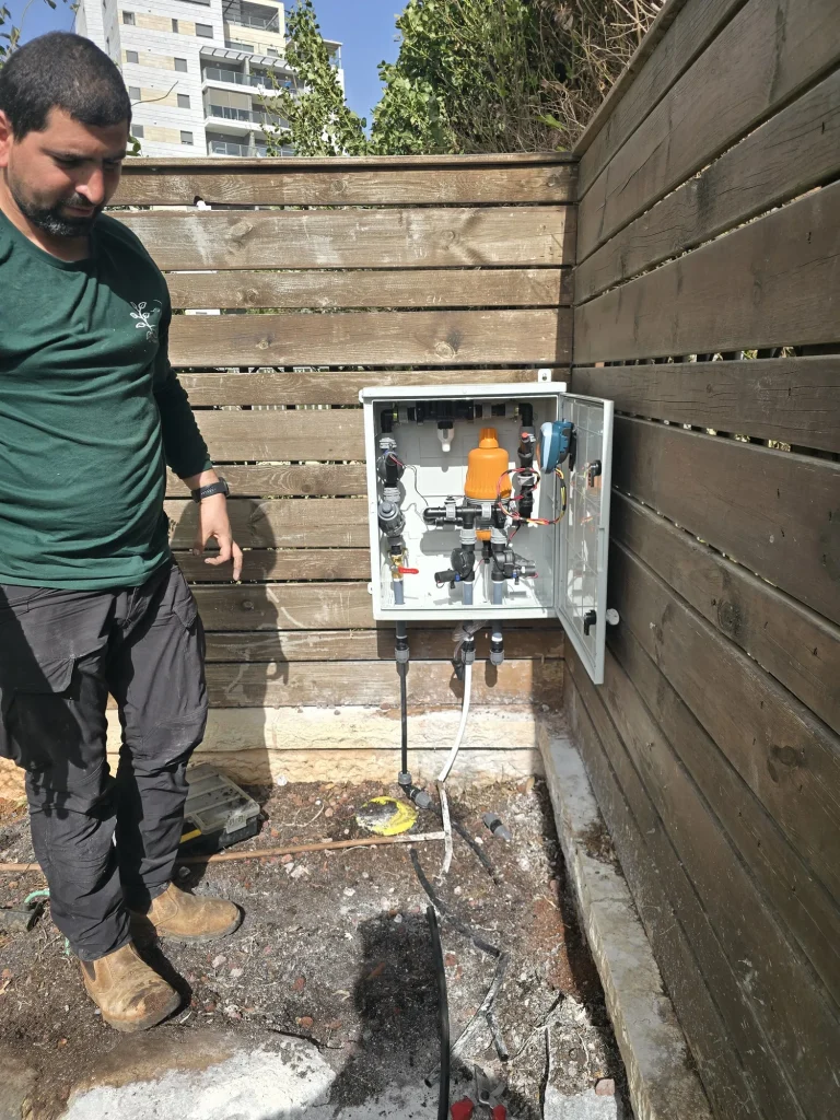 איש צוות מתקין ארון בקר השקיה ליד גדר העץ